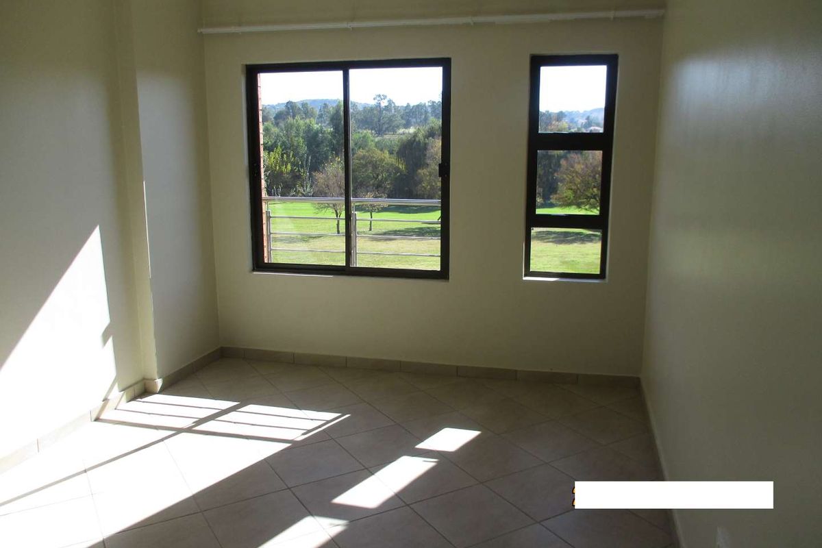 A bright, empty bedroom featuring tiled flooring, neutral walls, and large windows offering scenic views of the surrounding greenery.
