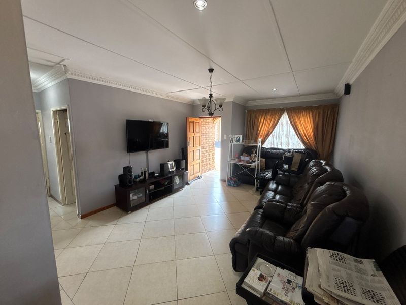 A spacious living room featuring tiled flooring, decorative ceiling cornices, and recessed lighting, providing a comfortable and functional area for relaxation.