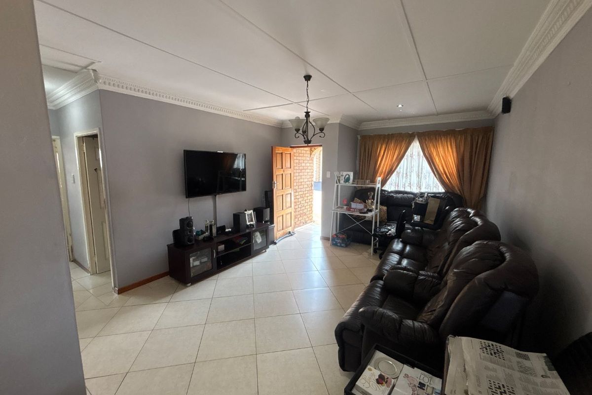 A spacious living room featuring tiled flooring, decorative ceiling cornices, and recessed lighting, providing a comfortable and functional area for relaxation.