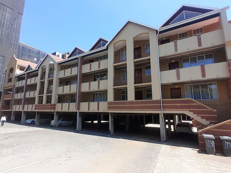 Exterior view of a multi-story apartment complex featuring brick facade, covered ground-level parking, and private balconies.