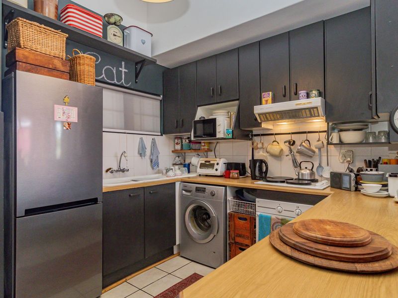 A compact kitchen featuring dark cabinetry, light wood-look countertops, tiled backsplash, and integrated laundry facilities, offering a functional and efficient workspace.