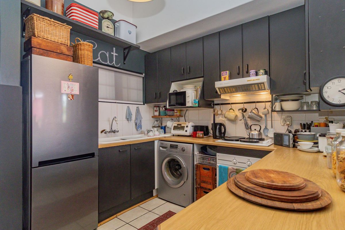 A compact kitchen featuring dark cabinetry, light wood-look countertops, tiled backsplash, and integrated laundry facilities, offering a functional and efficient workspace.