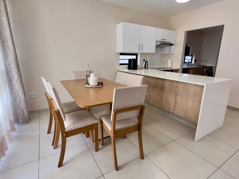 Open plan dining area featuring modern kitchen cabinetry, a functional island, and neutral tiled flooring, seamlessly connecting to the kitchen space.