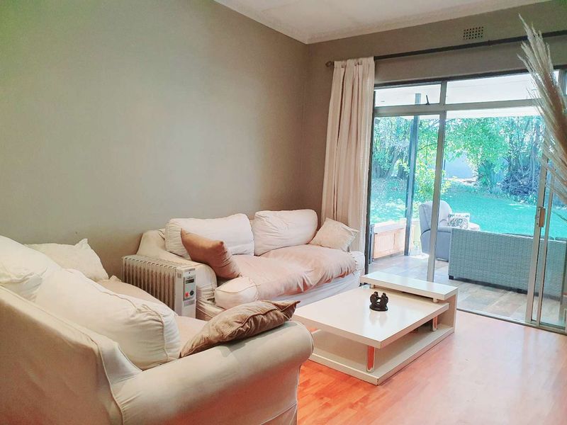 A comfortable living room featuring laminate flooring and large sliding glass doors that provide direct access to the outdoor patio and garden area.