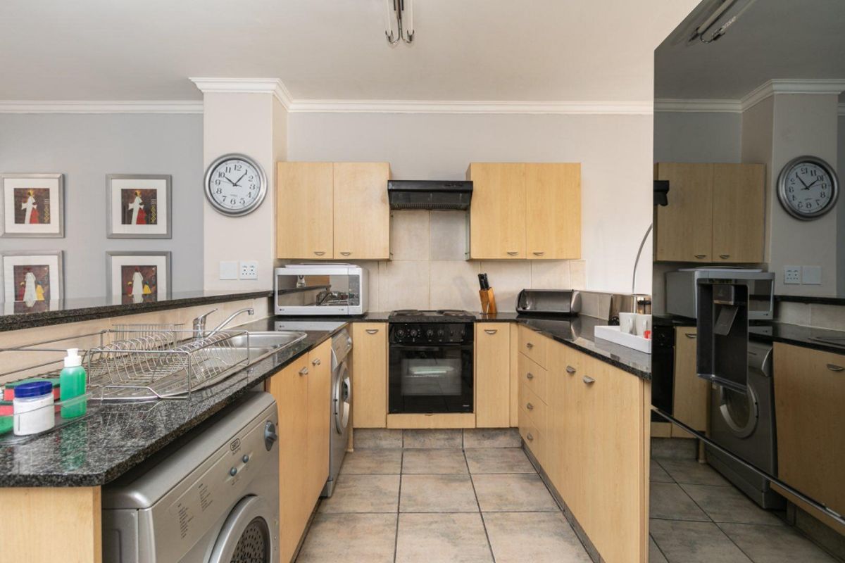 Functional kitchen featuring light wood cabinetry, dark granite countertops, integrated oven with extractor fan, and dedicated space for laundry appliances.