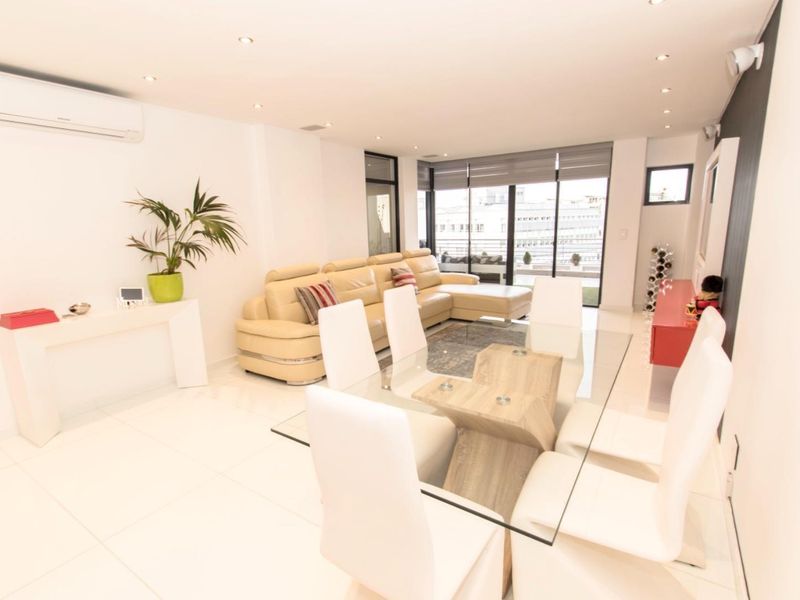 Bright open-plan living and dining area featuring large format floor tiles, recessed lighting, and direct access to a balcony through sliding glass doors.