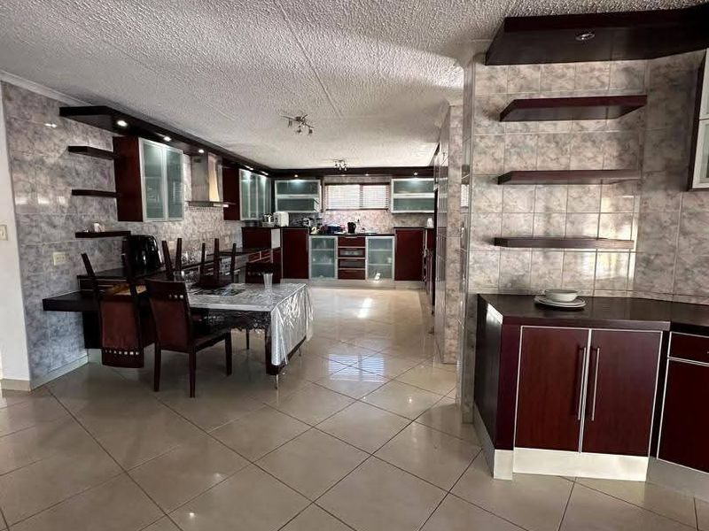 Spacious open-plan kitchen and dining area featuring extensive built-in cabinetry, tiled flooring, and integrated shelving, offering a functional layout for modern living.