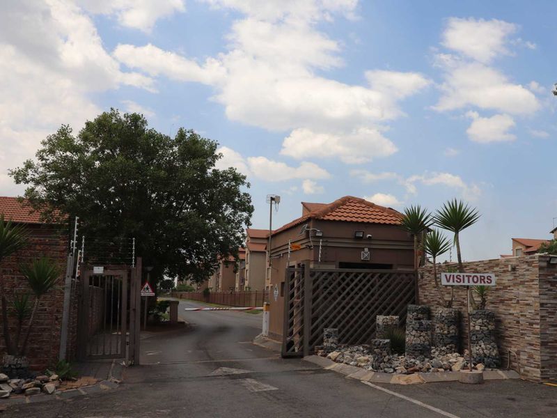 Secure residential complex entrance featuring a guard house, boom gate access, and stone-clad perimeter walls with electric fencing.