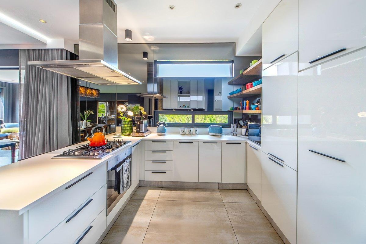 Modern kitchen featuring high-gloss white cabinetry, stone countertops, integrated appliances, a mirrored splashback, and a gas cooktop with a stainless steel extractor fan.