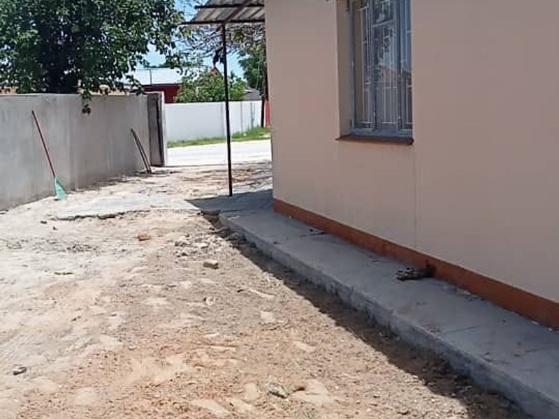 Side view of the property showing a concrete perimeter wall, metal window frames, and an unlandscaped dirt yard area.