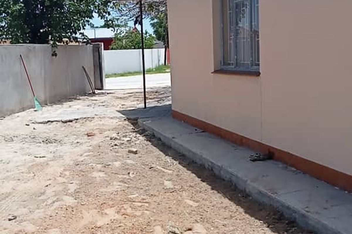 Side view of the property showing a concrete perimeter wall, metal window frames, and an unlandscaped dirt yard area.