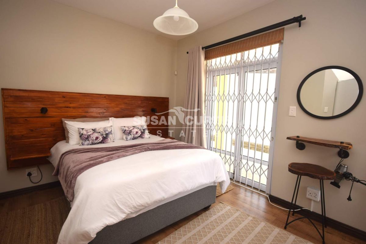 A well-maintained bedroom featuring a custom wooden headboard, laminate flooring, and a sliding glass door with security gate access to the exterior.