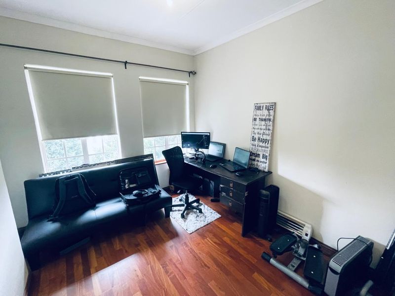 A functional home office space featuring laminate flooring and dual windows with roller blinds, offering a versatile area for work or study.