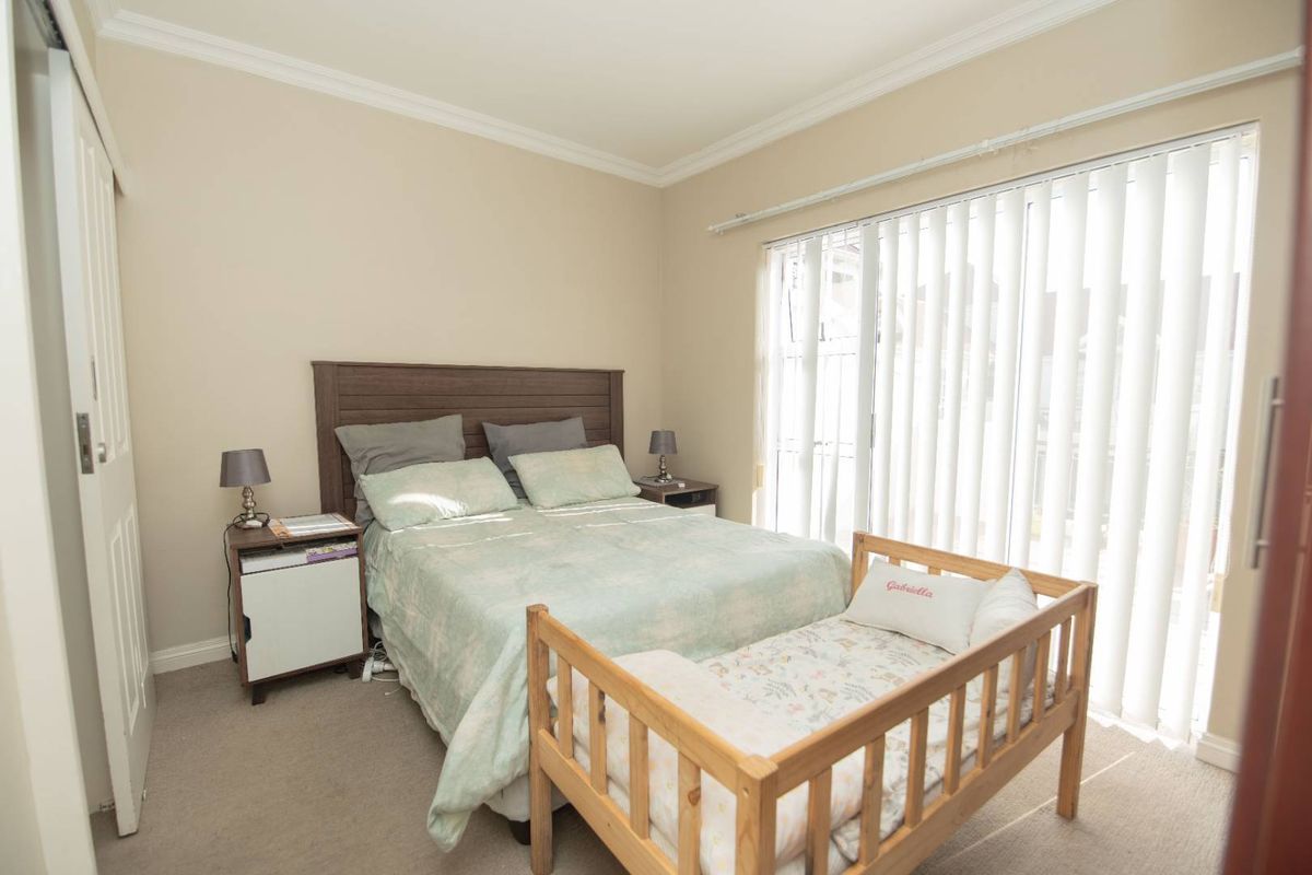 A carpeted bedroom featuring crown molding and a large sliding glass door with vertical blinds providing natural light.