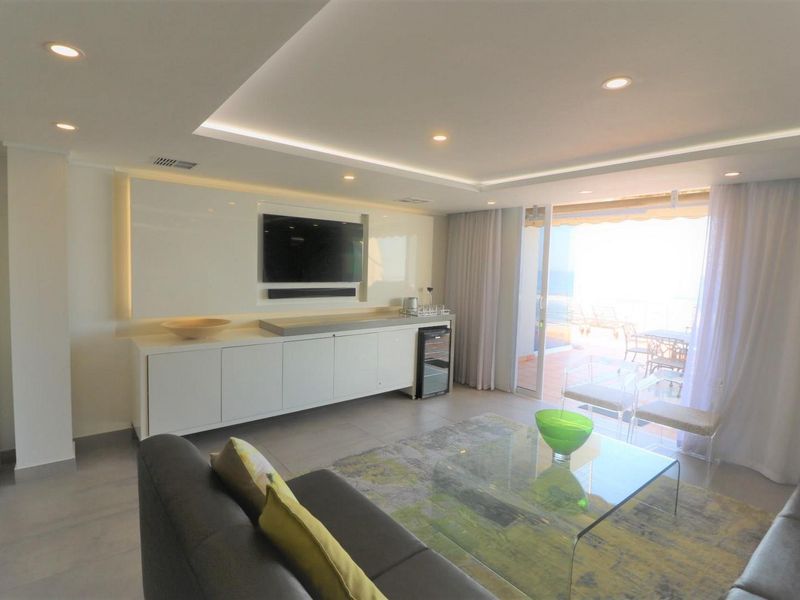 Modern living room featuring recessed cove lighting, sleek built-in cabinetry, and large sliding glass doors opening to a balcony with natural light.