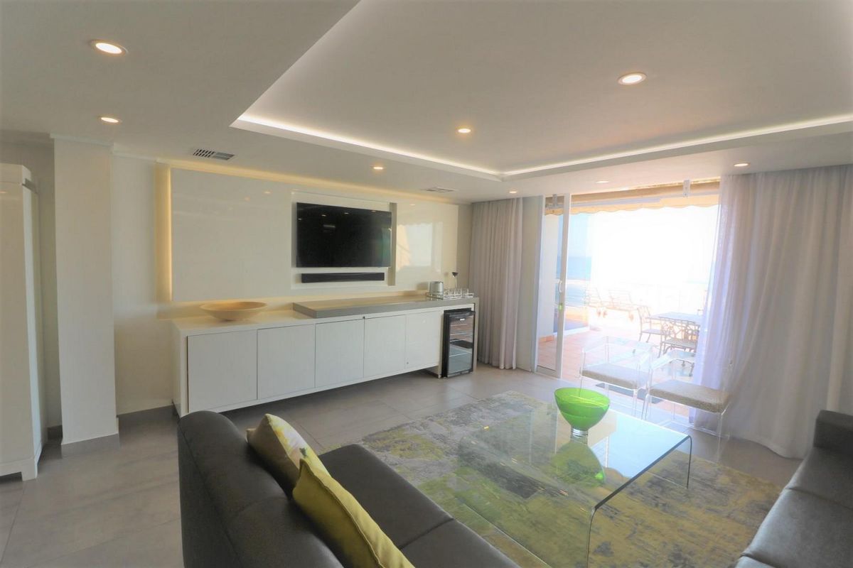 Modern living room featuring recessed cove lighting, sleek built-in cabinetry, and large sliding glass doors opening to a balcony with natural light.