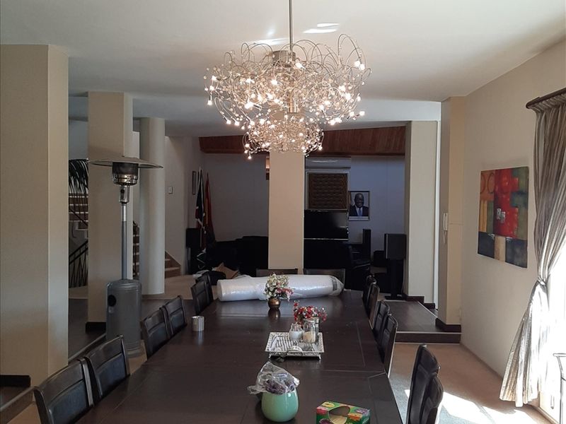 Spacious dining area featuring dual decorative chandeliers, structural columns, and neutral carpeting, providing an open-plan layout suitable for large gatherings.