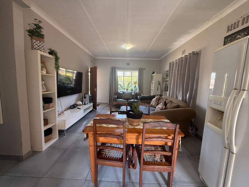An open-plan living and dining area featuring neutral wall tones, tiled flooring, and large windows allowing for natural light.