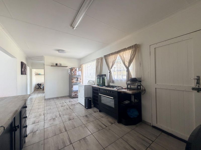 A functional kitchen area featuring tiled flooring, built-in cabinetry, and a gas stove with oven, leading into an adjacent living space.