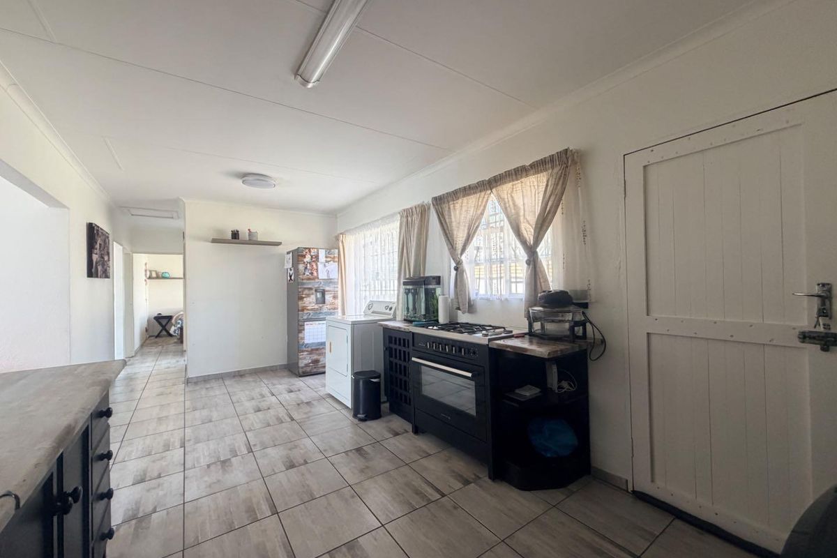 A functional kitchen area featuring tiled flooring, built-in cabinetry, and a gas stove with oven, leading into an adjacent living space.