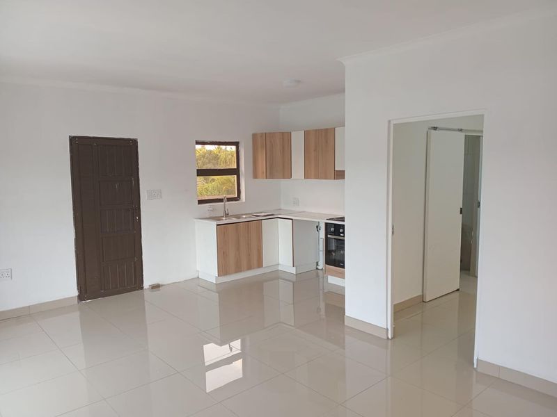 An open-plan living and kitchen area featuring modern cabinetry, built-in oven, ceramic tiled flooring, and neutral finishes throughout.