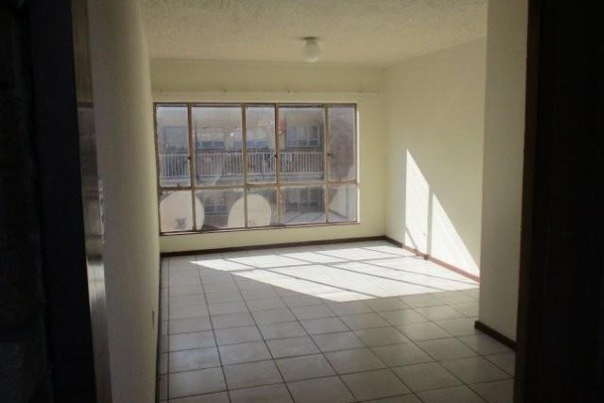 An empty, sunlit living area featuring tiled flooring and a large window, offering a blank canvas for potential interior design updates.