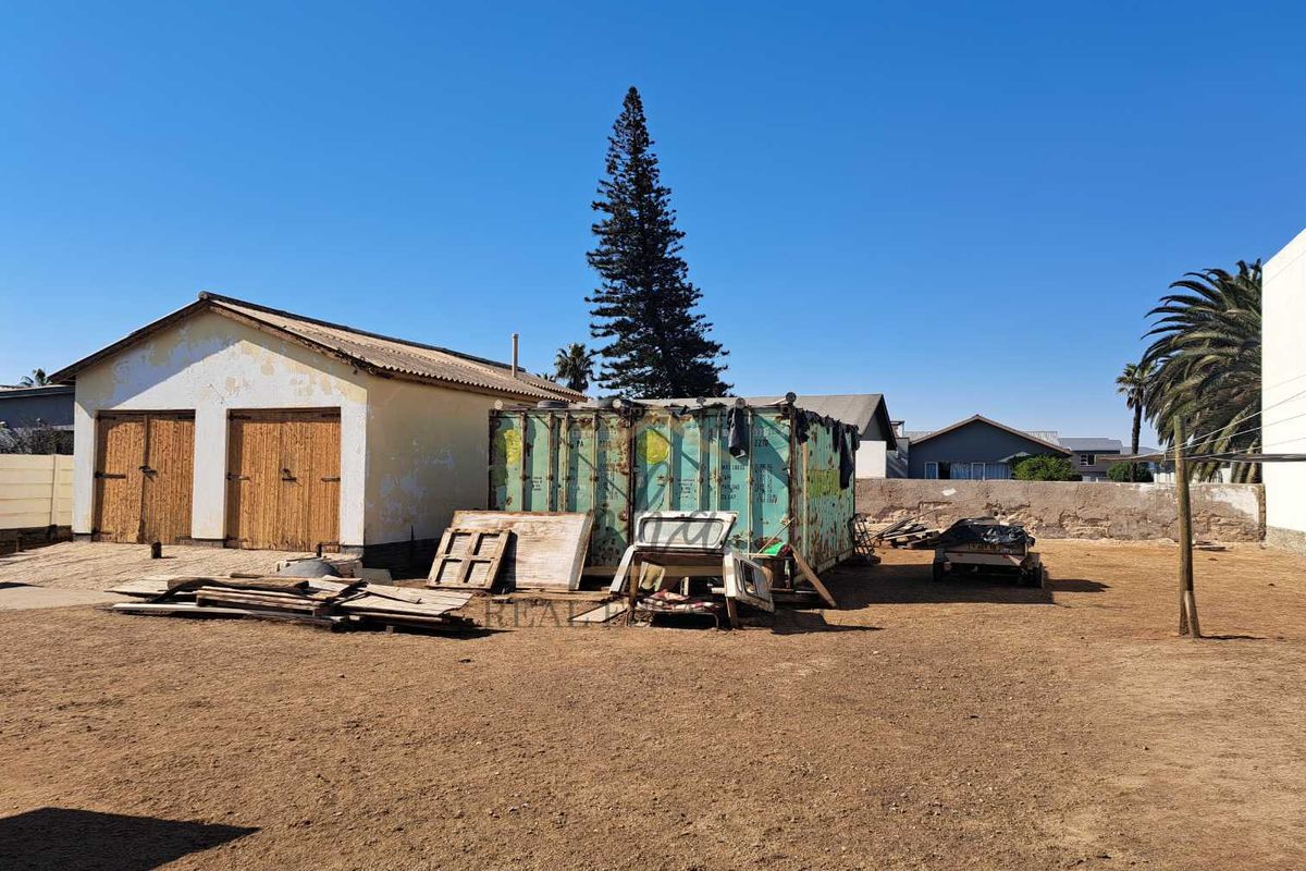 Rear yard area featuring a detached garage structure with visible exterior wear and a large open plot with boundary walling.