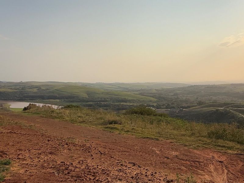 A scenic view overlooking rolling hills and a distant water body from an elevated, undeveloped residential land plot.