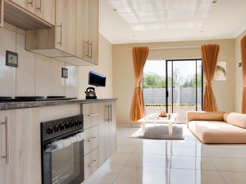 Modern open-plan living area featuring a contemporary kitchen with light wood cabinetry, integrated oven, and seamless flow to the outdoor space via sliding doors.