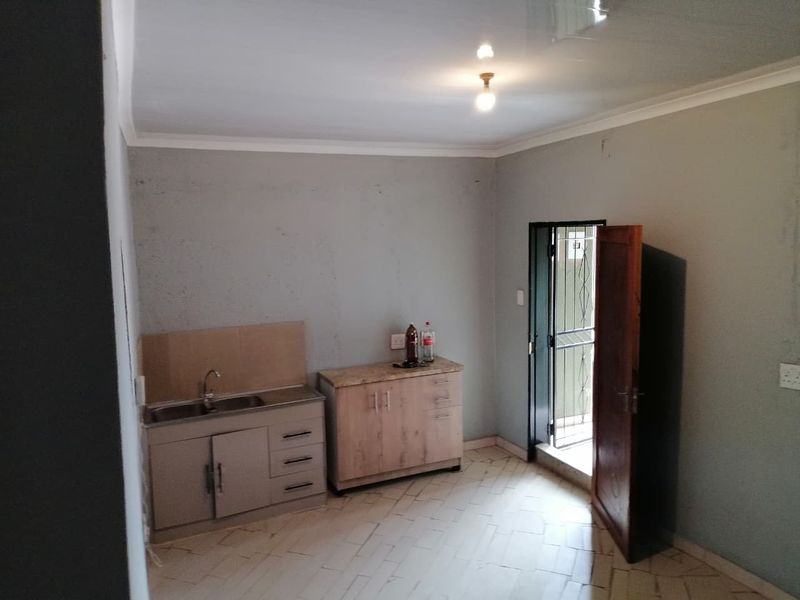 A compact, empty kitchen area featuring basic cabinetry, a stainless steel sink, and tiled flooring, with direct access to an exterior door.