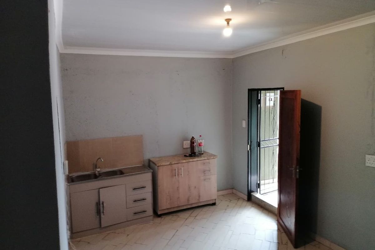 A compact, empty kitchen area featuring basic cabinetry, a stainless steel sink, and tiled flooring, with direct access to an exterior door.
