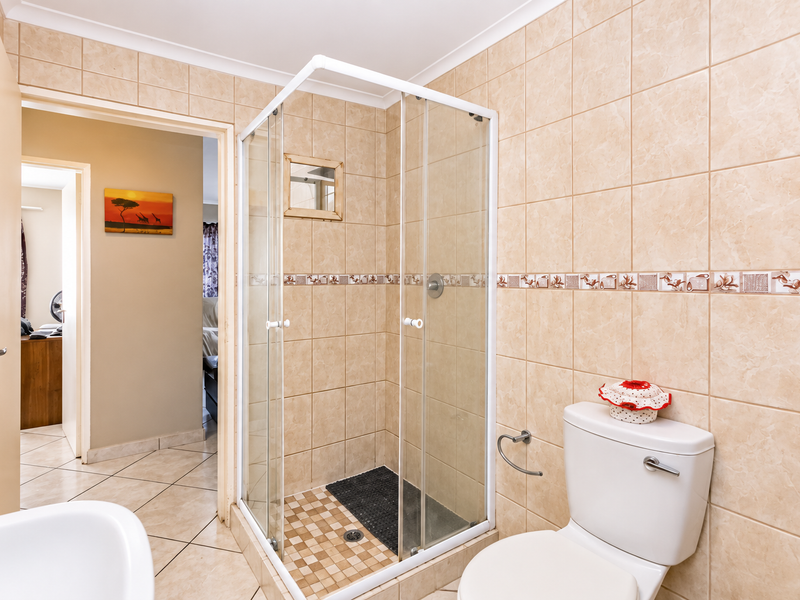 A functional bathroom featuring a glass shower enclosure, ceramic wall and floor tiling, and a standard toilet suite.