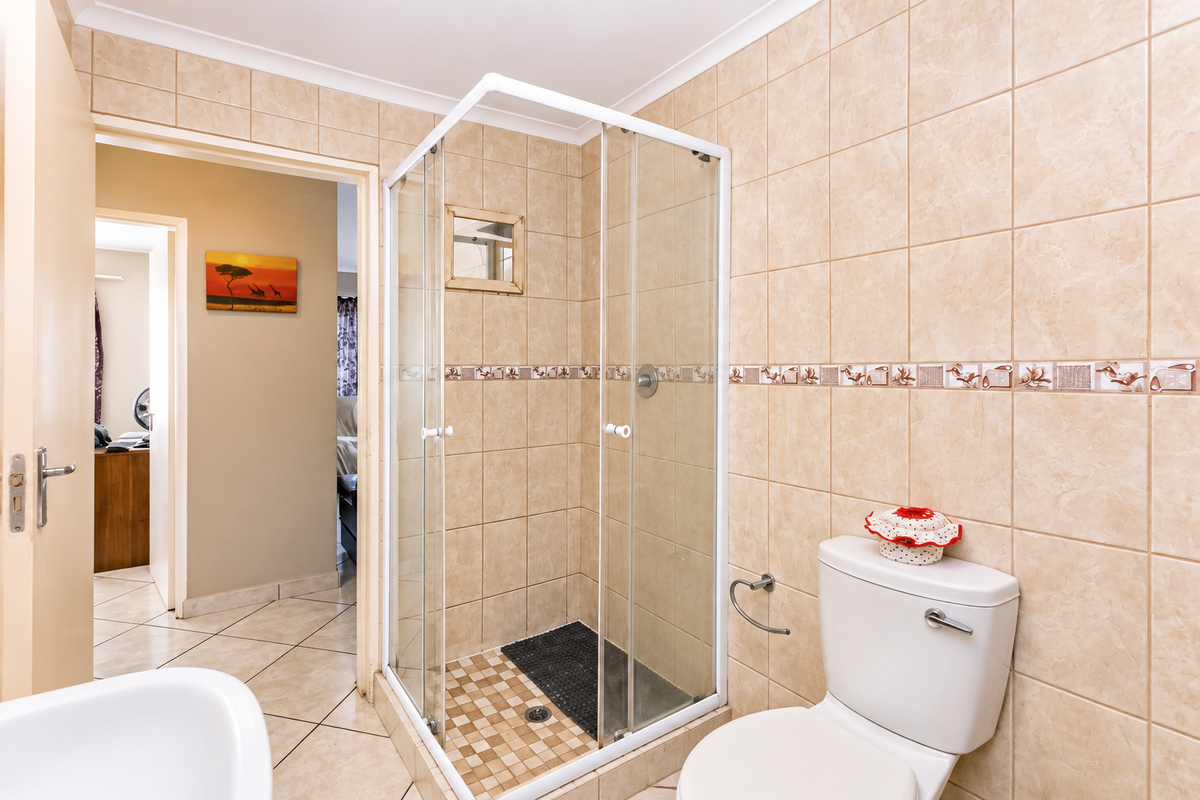 A functional bathroom featuring a glass shower enclosure, ceramic wall and floor tiling, and a standard toilet suite.