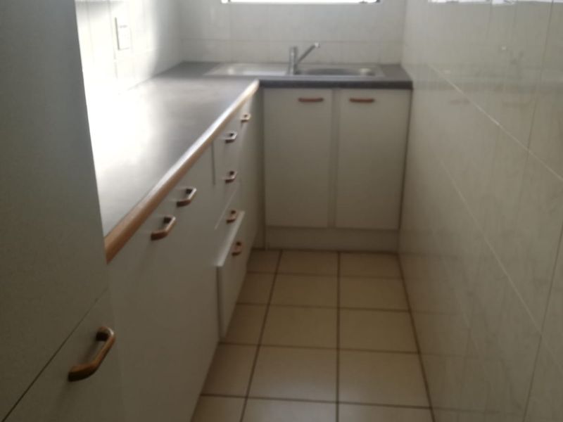 A compact, functional kitchen featuring white built-in cabinetry, tiled walls, and tiled flooring, providing a clean and practical workspace.