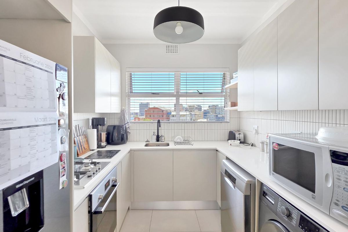 Modern galley-style kitchen featuring sleek white cabinetry, quartz countertops, integrated appliances, and a tiled backsplash with a window view.