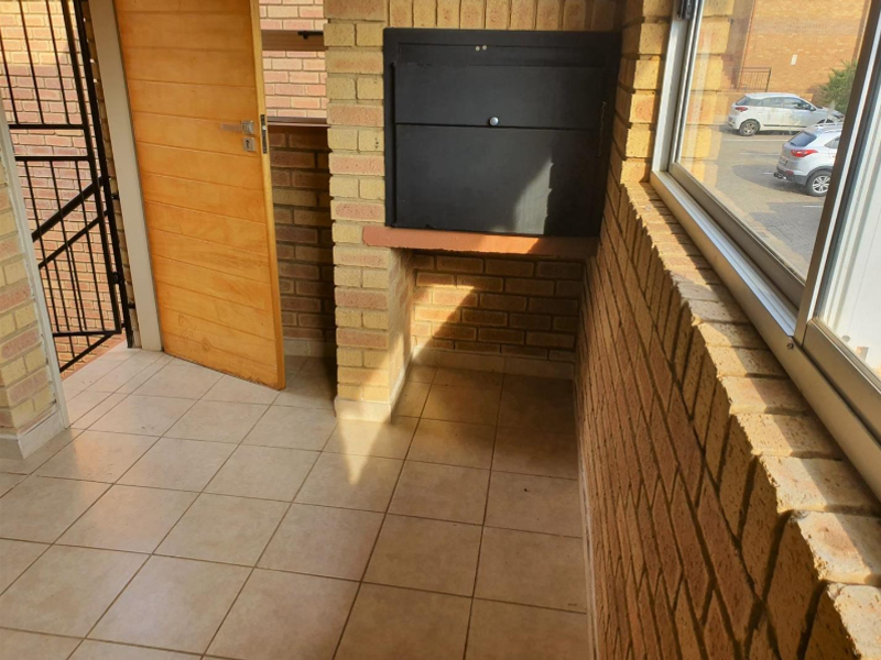 Covered balcony area featuring facebrick walls, tiled flooring, and a built-in braai unit, offering a functional outdoor entertainment space.