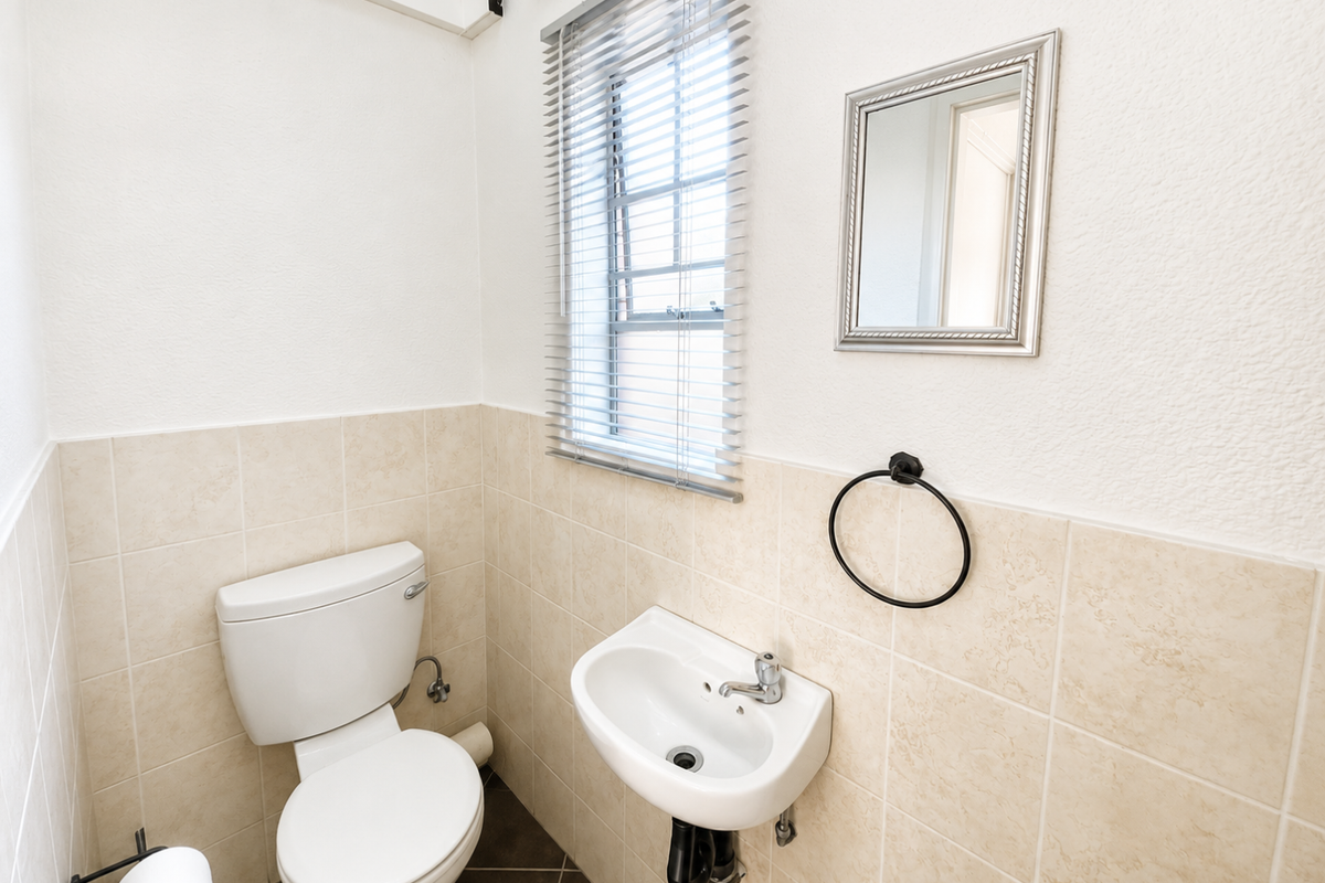 A clean and functional guest bathroom featuring a wall-mounted basin, toilet, neutral wall tiling, and a window with venetian blinds.