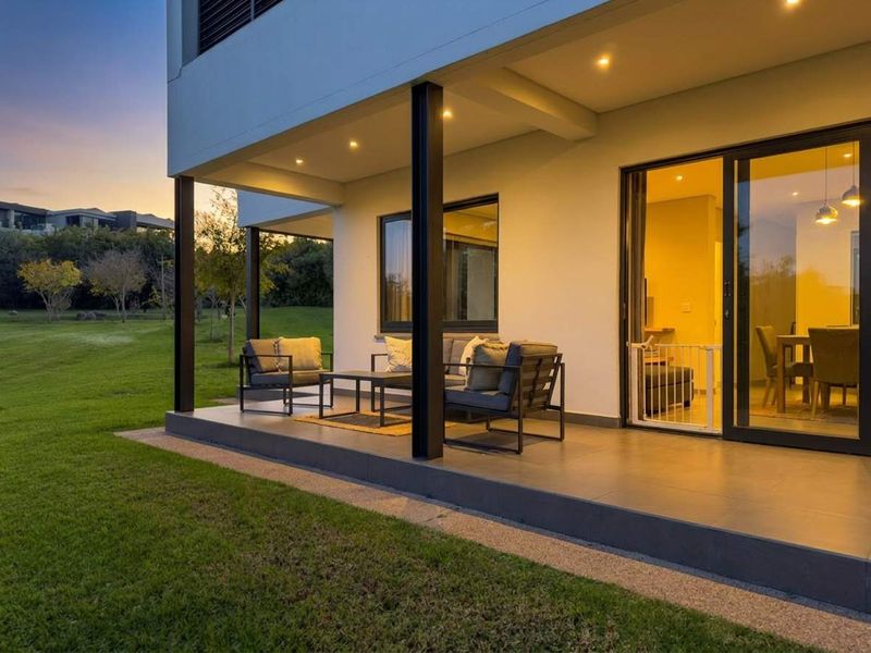 A modern covered patio featuring tiled flooring, recessed lighting, and black structural columns, providing seamless indoor-outdoor flow through large sliding glass doors.