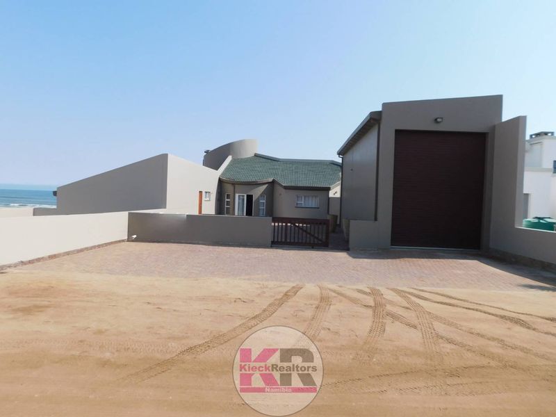 Front exterior view of the property featuring a paved driveway, a secure garage with a roller shutter door, and a boundary wall.