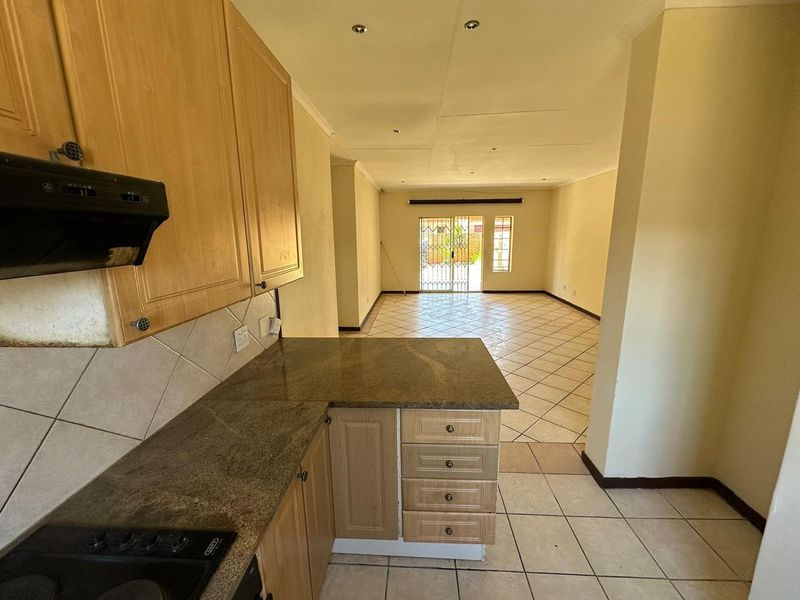 Open-plan kitchen and living area featuring tiled floors, granite countertops, and built-in cabinetry, leading to a secure rear entrance.