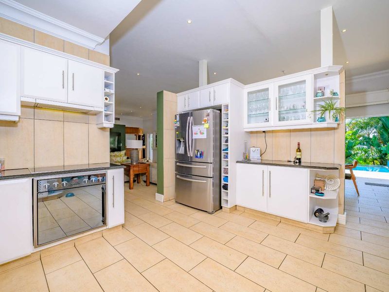 Spacious open-plan kitchen featuring white cabinetry, granite countertops, and integrated appliances, flowing seamlessly into the living area with views of the outdoor pool.