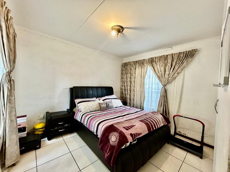 A bedroom featuring tiled flooring and a central ceiling light fixture, showing signs of wear on the wall surfaces.