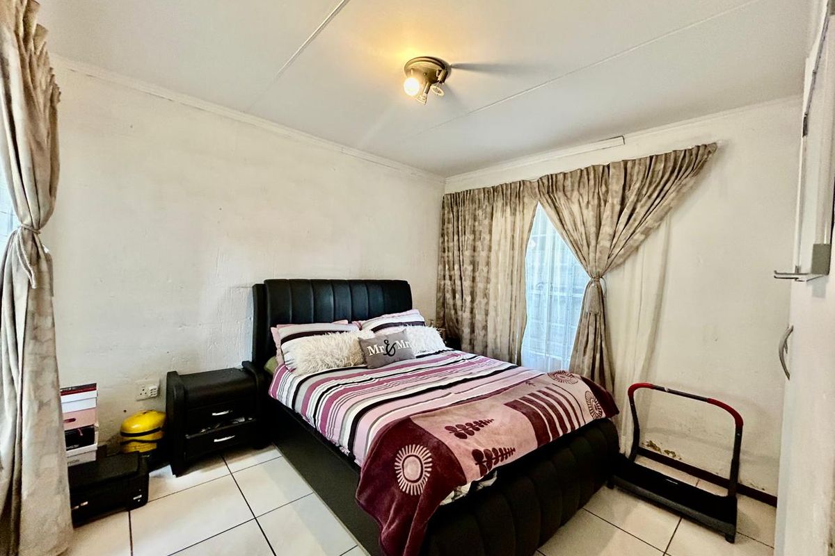 A bedroom featuring tiled flooring and a central ceiling light fixture, showing signs of wear on the wall surfaces.