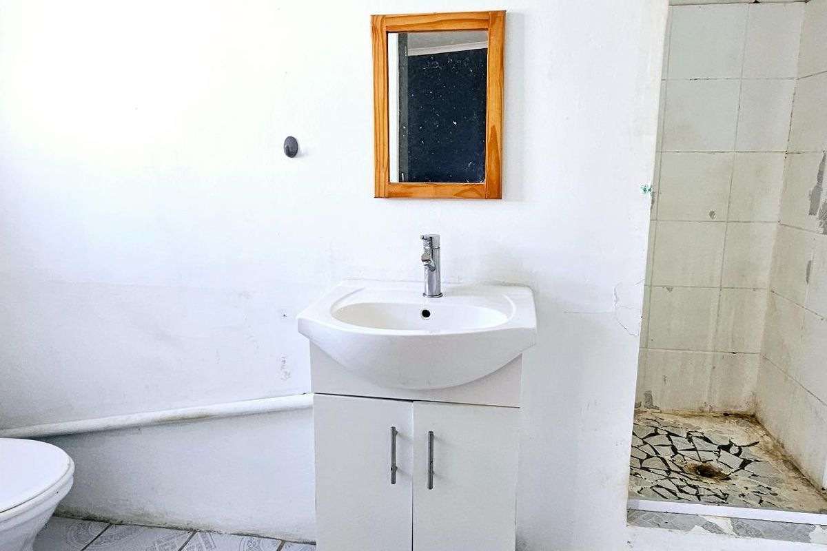 A dated bathroom featuring a vanity basin, toilet, and a shower enclosure with visible wear to the wall finishes and flooring.