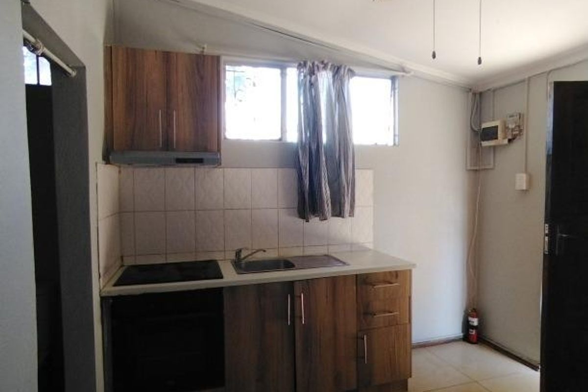 A compact kitchen featuring built-in cabinetry, an electric hob, oven, and tiled splashback, offering a functional layout ready for modernization.