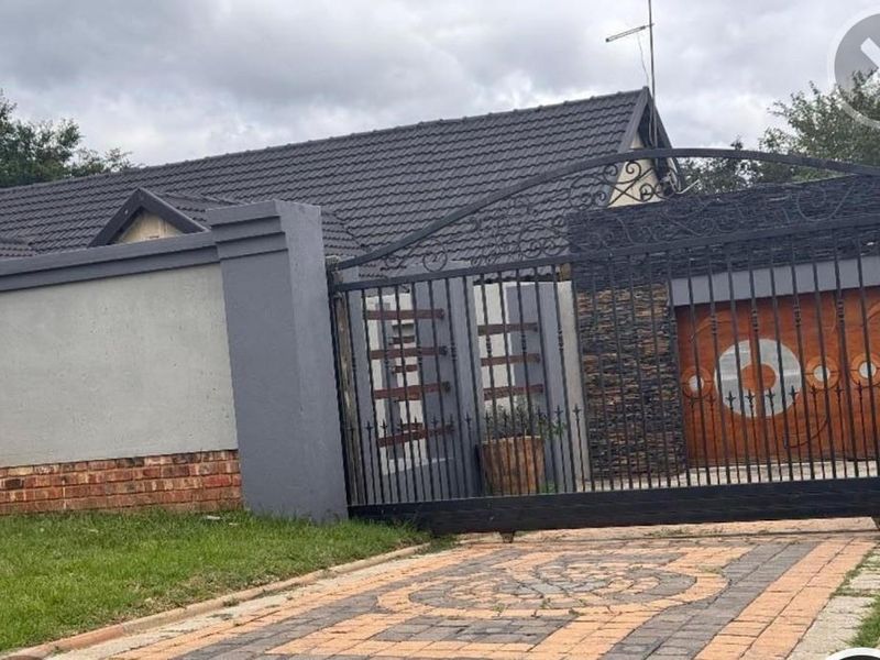 Front view of the property featuring a secure wrought iron gate, paved driveway, and a well-maintained perimeter wall with stone cladding accents.