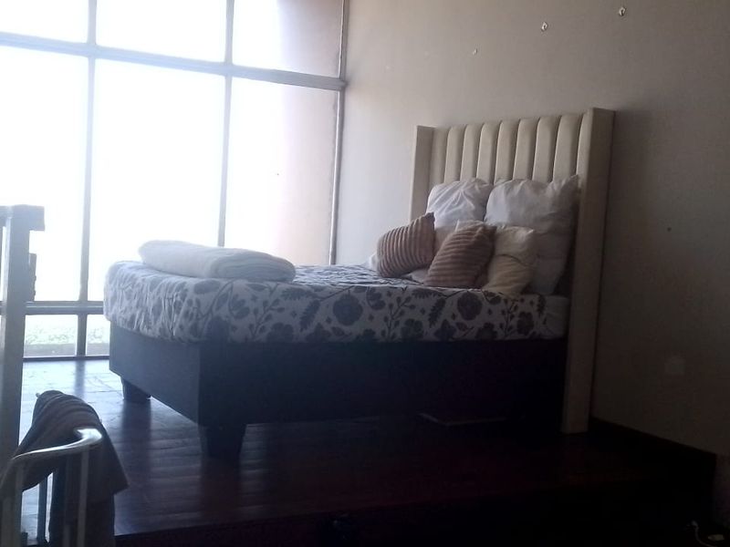 A mezzanine bedroom area featuring a raised wooden platform, a protective balustrade, and expansive floor-to-ceiling windows providing ample natural light.