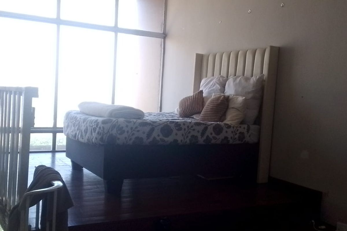 A mezzanine bedroom area featuring a raised wooden platform, a protective balustrade, and expansive floor-to-ceiling windows providing ample natural light.