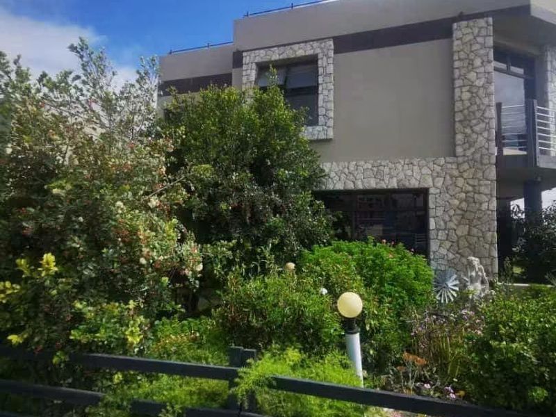 Front elevation of a modern multi-story house featuring stone cladding accents, a balcony, and established garden landscaping.