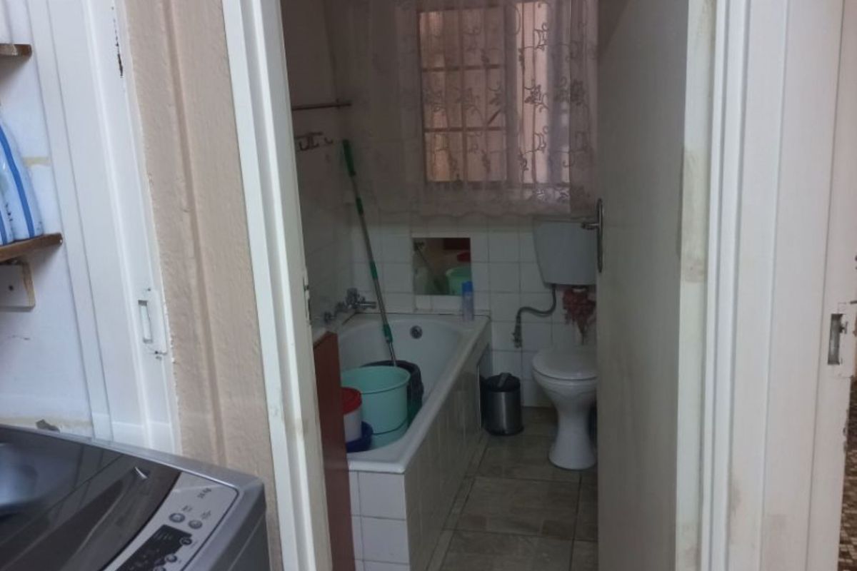 A compact bathroom featuring a bathtub, toilet, and tiled flooring, viewed from an adjacent laundry area.